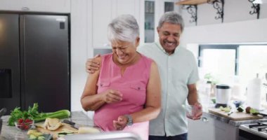 Happy senior biracial couple preparing healthy drink in kitchen. Spending quality time at home, retirement and lifestyle concept.