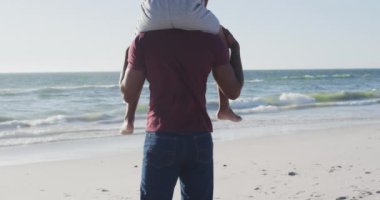 Video of african american father carrying son on arms and walking on beach. Holidays, vacations, relations and spending quality family time together concept.