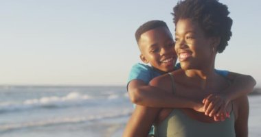 Mutlu Afro-Amerikan anne ve oğlunun gün batımında sahilde eğlendiği bir video. Tatiller, tatiller, rahatlamak ve ailece sahilde güzel vakit geçirmek..