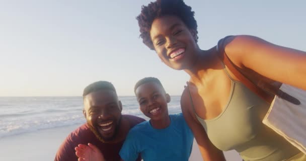 日没時にビーチでビデオ通話をしている幸せなアフリカ系アメリカ人の家族のビデオ リラックスしてビーチで質の高い家族の時間を過ごす — ストック動画
