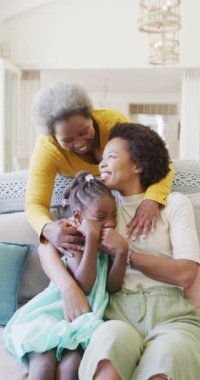 Afro-Amerikan anne, kız ve büyükannenin evde kucaklaştığı dikey video, yavaş çekim. Mutluluk, aile, birliktelik ve aile hayatı kavramı..