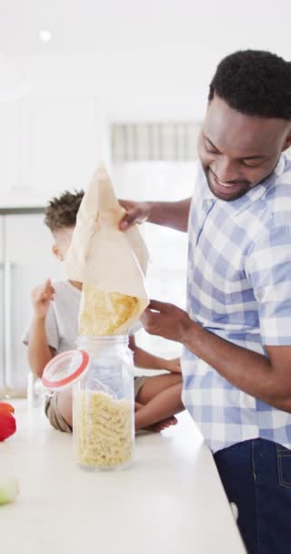 笑顔アフリカ系アメリカ人の父親と息子がパスタで瓶を充填する垂直ビデオ スローモーション 団結と国内生活の概念 — ストック動画