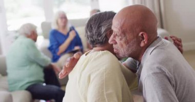 Senior biracial man hugging sad diverse senior female friend at support group, slow motion. Friendship, support and senior lifestyle.