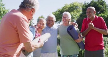 Diverse group of happy male and female seniors talking after exercising in sunny garden, slow motion. Friendship and healthy, active senior lifestyle.