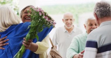 Happy couple greeting group of diverse senior male and female friends at front door, slow motion. Friendship, relaxation and senior lifestyle.