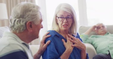 Distressed senior caucasian woman talking to male friends in living room, slow motion. Friendship, support and senior lifestyle.