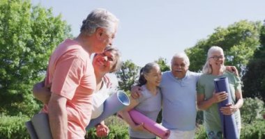 Diverse group of happy male and female seniors talking after exercising in sunny garden, slow motion. Friendship and healthy, active senior lifestyle.
