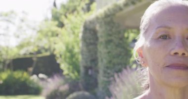 Half face portrait of happy senior asian woman smiling in garden, copy space, in slow motion. Healthy, active senior lifestyle.