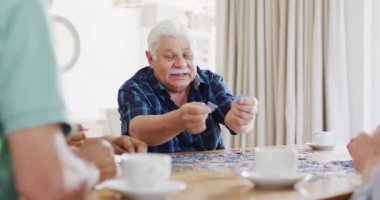 Happy senior caucasian man doing jigsaw puzzle at home with diverse senior friends, slow motion. Friendship, relaxation and senior lifestyle.