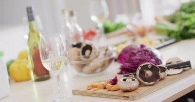 Glasses of white wine and fresh vegetables on chopping board on kitchen counter top, slow motion. Food, drink, entertaining and domestic lifestyle.