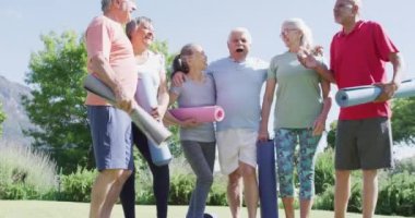 Diverse group of happy male and female seniors talking after exercising in sunny garden, slow motion. Friendship and healthy, active senior lifestyle.