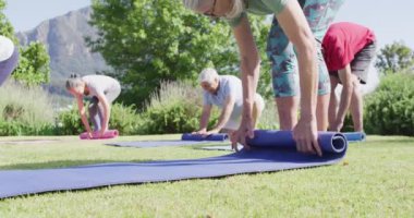 Diverse group of male and female seniors rolling up yoga mats after exercise in garden, slow motion. Healthy, active senior lifestyle.