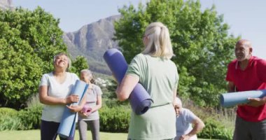 Diverse group of happy male and female seniors talking after exercising in garden, slow motion. Friendship and healthy, active senior lifestyle.