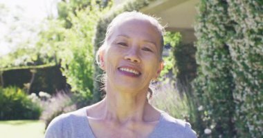 Portrait of happy senior asian woman smiling in garden, in slow motion. Healthy, active senior lifestyle.