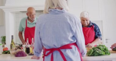 Happy group of diverse senior male and female friends preparing food in kitchen, slow motion. Friendship, cooking and active senior lifestyle.