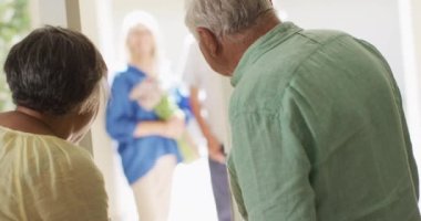 Happy diverse couple greeting group of senior male and female friends at front door, slow motion. Friendship, relaxation and senior lifestyle.