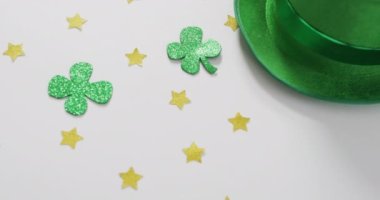 Shamrocks and stars with green hat with copy space on white background. Irish tradition and st patrick's day celebration concept digitally generated video.