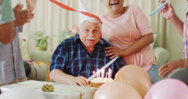 Happy senior caucasian man having birthday party and cake with diverse senior friends, slow motion. Friendship, celebration and senior lifestyle.