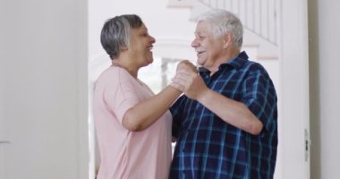 Happy diverse senior couple having fun dancing together at home, slow motion. Friendship, togetherness and senior lifestyle.
