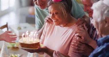 Happy senior caucasian woman having birthday party and cake with diverse senior friends, slow motion. Friendship, celebration and senior lifestyle.