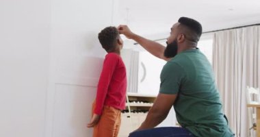 Mutlu Afro-Amerikan baba ve oğlu yavaş çekimde boy ölçüyorlar. Kaliteli zaman geçirme, ev hayatı ve çocukluk kavramı.