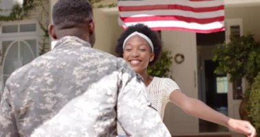 Mutlu Afro-Amerikan erkek askeri yavaş çekimde karısını Amerikan bayrağıyla kucaklıyor. Yurtseverlik kavramında kaliteli zaman geçirmek.
