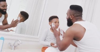 Afro-Amerikan baba ve oğlu banyoda yüzüne tıraş kremi sürüyorlar, yavaş çekimde. Kaliteli zaman geçirme, ev hayatı ve çocukluk kavramı.