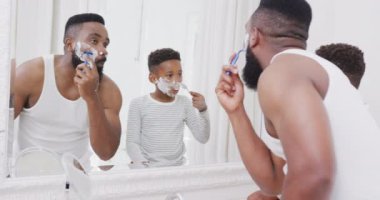 Afro-Amerikan baba ve oğlu banyoda sakallarını yavaş çekimde tıraş ederken mutlu olun. Kaliteli zaman geçirme, ev hayatı ve çocukluk kavramı.
