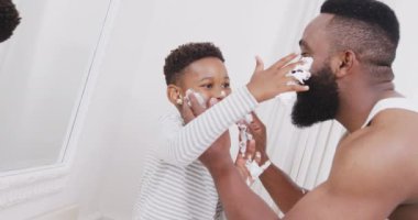 Afro-Amerikan baba ve oğlu banyoda yüzüne tıraş kremi sürüyorlar, yavaş çekimde. Kaliteli zaman geçirme, ev hayatı ve çocukluk kavramı.