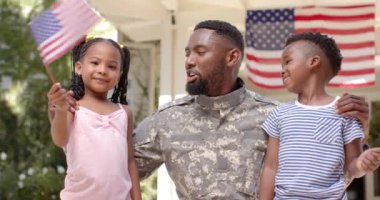 Mutlu Afro-Amerikan erkek askeri çocuklarını Amerikan bayraklarıyla kucaklıyor, ağır çekimde. Yurtseverlik kavramında kaliteli zaman geçirmek.