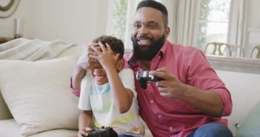 Mutlu Afro-Amerikan baba ve oğlu ağır çekimde video oyunları seyrediyor. Kaliteli zaman geçirme, ev hayatı ve çocukluk kavramı.