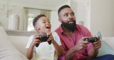 Mutlu Afro-Amerikan baba ve oğlu ağır çekimde video oyunları seyrediyor. Kaliteli zaman geçirme, ev hayatı ve çocukluk kavramı.