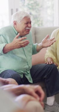 Vertical video of distressed senior caucasian man talking with friends in living room, slow motion. Friendship, support and senior lifestyle.