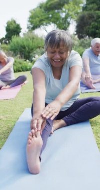 Vertical video of happy diverse senior men and women doing yoga in sunny garden, in slow motion. Healthy, active senior lifestyle.
