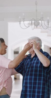 Vertical video of diverse senior couple having fun dancing at home, slow motion. Romance, togetherness and senior lifestyle.