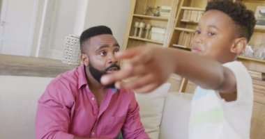 Ciddi Afro-Amerikan baba ve oğlu koltukta oturup ağır çekimde konuşuyorlar. Kaliteli zaman geçirme, ev hayatı ve çocukluk kavramı.