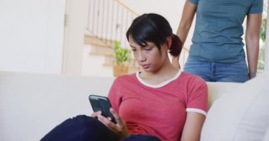 Çift ırklı kız kardeşler koltukta oturup akıllı telefon kullanıyor, ağır çekimde. Kaliteli zaman, yaşam tarzı, aile hayatı, aile ve kardeş kavramı.