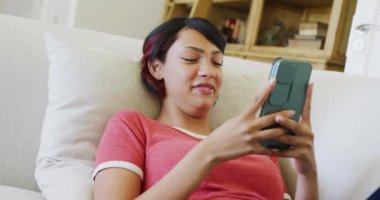 Kanepede oturan ve akıllı telefonu yavaş çekimde kullanan melez genç kız. Kaliteli zaman, yaşam tarzı, ev hayatı, ergenlik kavramı.