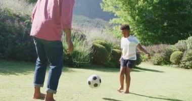 Mutlu Afro-Amerikan baba ve oğlu bahçede yavaş çekimde futbol oynuyor. Kaliteli zaman geçirme, ev hayatı ve çocukluk kavramı.