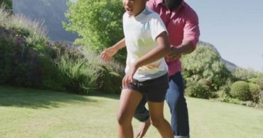 Mutlu Afro-Amerikan baba ve oğlu bahçede yavaş çekimde futbol oynuyor. Kaliteli zaman geçirme, ev hayatı ve çocukluk kavramı.