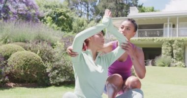 Çift ırklı kız kardeşler yoga yapıyor ve bahçede yavaş çekimde meditasyon yapıyor. Kaliteli zaman, yaşam tarzı, aile hayatı, aile ve kardeş kavramı.