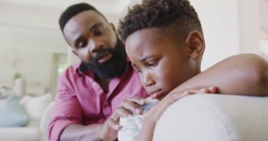 Üzgün Afro-Amerikan baba ve oğlu kanepede oturuyor ve yavaş çekimde kucaklaşıyorlar. Kaliteli zaman geçirme, ev hayatı ve çocukluk kavramı.