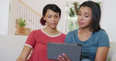 Kanepede oturan ve tablet kullanan mutlu melez kardeşler. Ağır çekimde. Kaliteli zaman, yaşam tarzı, aile hayatı, aile ve kardeş kavramı.