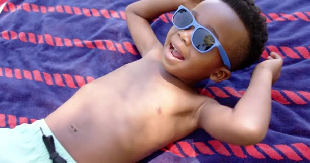 Glücklicher Afrikanisch Amerikanischer Junge Mit Sonnenbrille Auf Handtuch Liegend Zeitlupe — Stockvideo