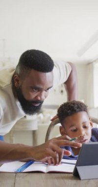 Afrika kökenli Amerikalı baba ve oğlunun birlikte ağır çekimde ödev yaptığı dikey bir video. Kaliteli zaman geçirme, ev hayatı ve çocukluk kavramı.