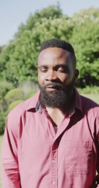 Yavaş çekimde gülümseyen Afrikalı Amerikalı bir adamın portresinin dikey videosu. Kaliteli zaman geçirme, ev hayatı