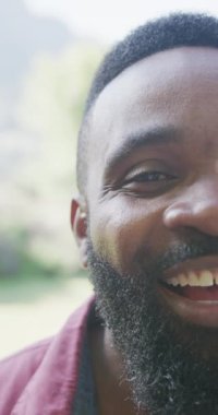 Yavaş çekimde gülümseyen Afrikalı Amerikalı bir adamın portresinin dikey videosu. Kaliteli zaman geçirme, ev hayatı 