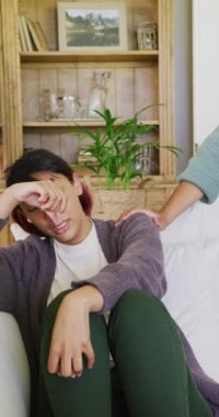 Çift ırklı kız kardeşlerin kanepede oturup kucaklaşmalarını gösteren dikey bir video. Kaliteli zaman, yaşam tarzı, aile hayatı, aile ve kardeş kavramı.