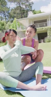 Çift ırklı kız kardeşlerin yoga yaptığı ve bahçede yavaş çekimde meditasyon yaptığı dikey bir video. Kaliteli zaman, yaşam tarzı, aile hayatı, aile ve kardeş kavramı.
