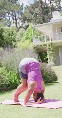Bahçede yoga yapan melez bir kadının dikey videosu, ağır çekimde. Kaliteli zaman, yaşam tarzı, aile hayatı, aile ve kardeş kavramı.